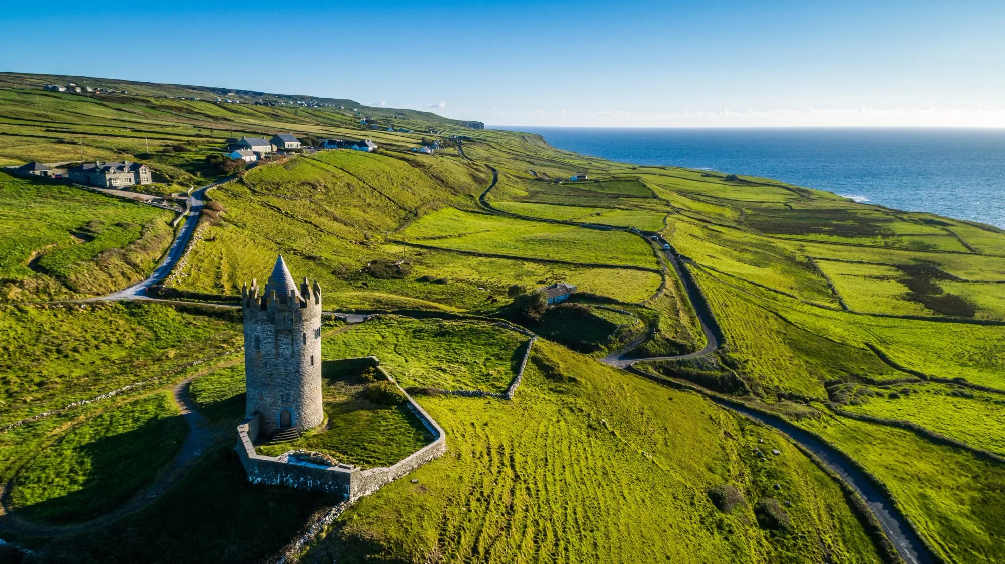 A castle in a lush green field overlooking the ocean in Ireland.