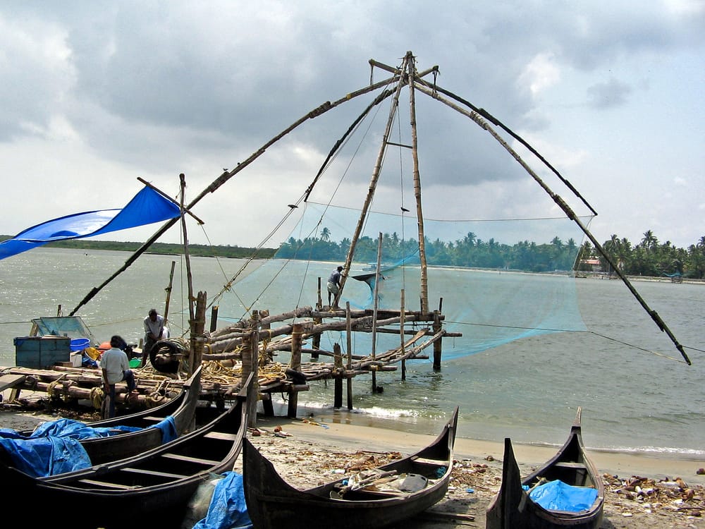 Fisherman in Kochi India at the edge of the river with fishing nets and boats.