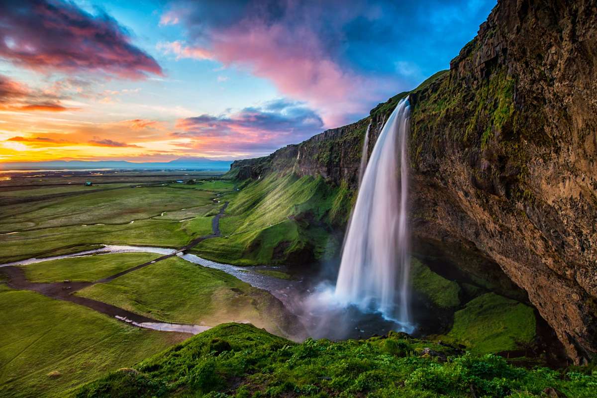 Powerful waterfall falling off a mountain in Iceland with bright green grass below.