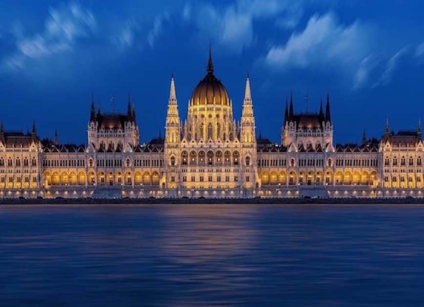 Nighttime view of the Budapest Parliament Building lit up on the river front of the Danube River. 