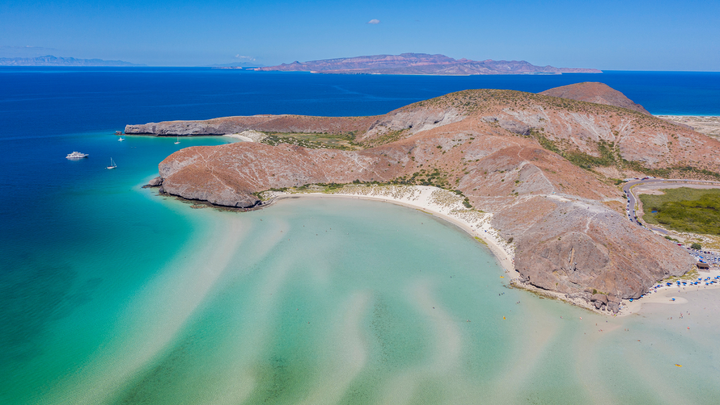 Ariel view of a mountainous island with a white sand beach surrounded by beautiful clear blue waters.