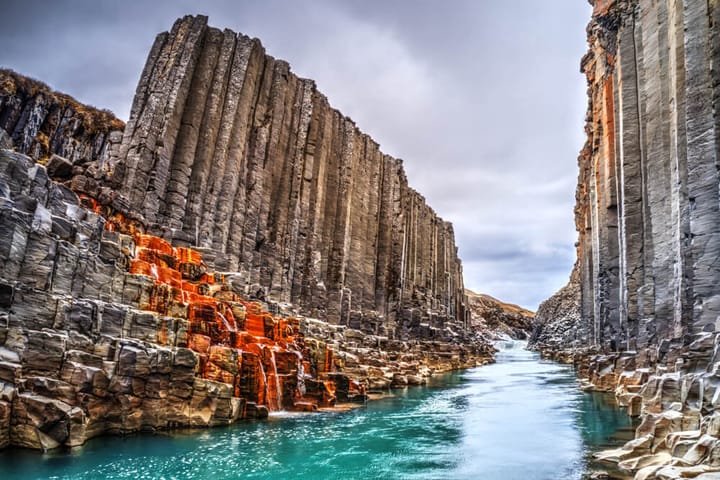 Dramatic view of Stuðlagil Canyon in Iceland, featuring towering basalt column cliffs and vibrant turquoise glacial river water.