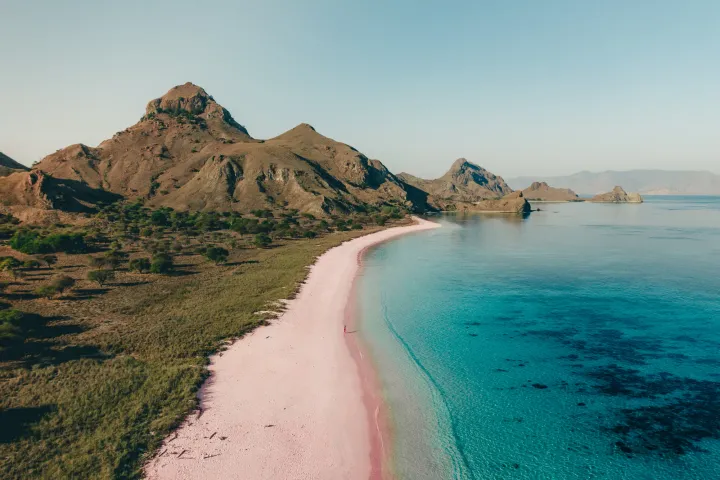 A pink beach at Komodo National Park, with beautiful clear blue waters and mountains in the background.