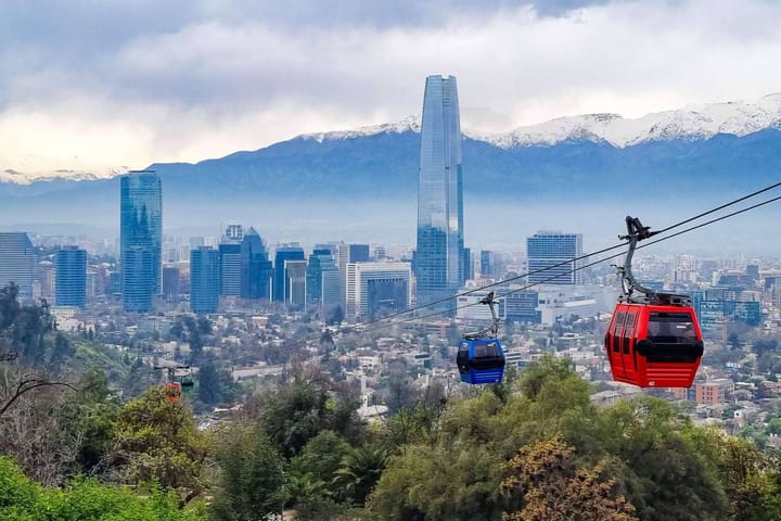 Santiago city skyline with mountain peaks in the background and red and blue gondola taking people up and down the mountain.