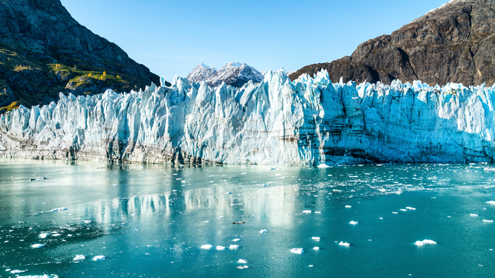 Icebergs floating in clear blue waters in Alaska with mountains in the background.