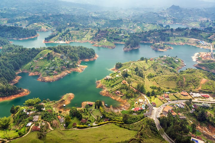 Ariel view of Guatape Lake in Colombia surrounded by lush green fields and forrest.