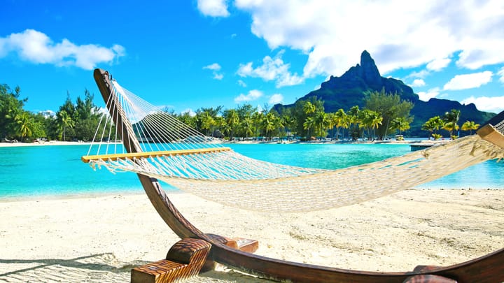 A hammock on the beach in Bora Bora with beautiful blue waters and mountain views.