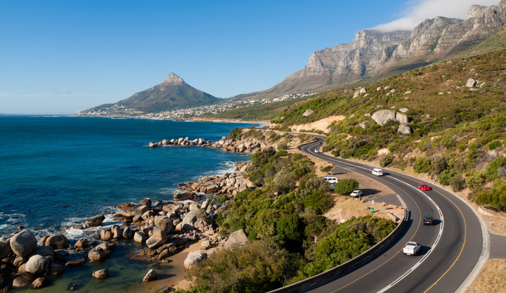 The Garden Route road in Cape Town, South Africa winds next to the ocean between the mountains.