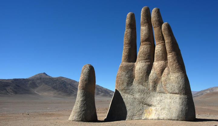 A giant hand sculpture in the middle of a dry desert located inside Atacama Desert in Chile.