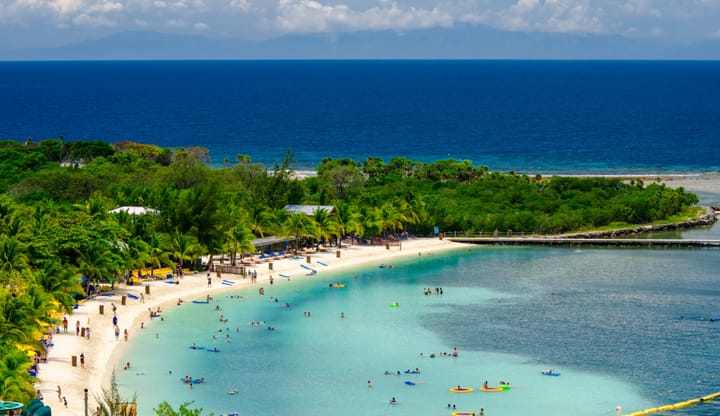 People playing on a beautiful beach with clear blue waters at Mahogany Bay beach resort, Honduras