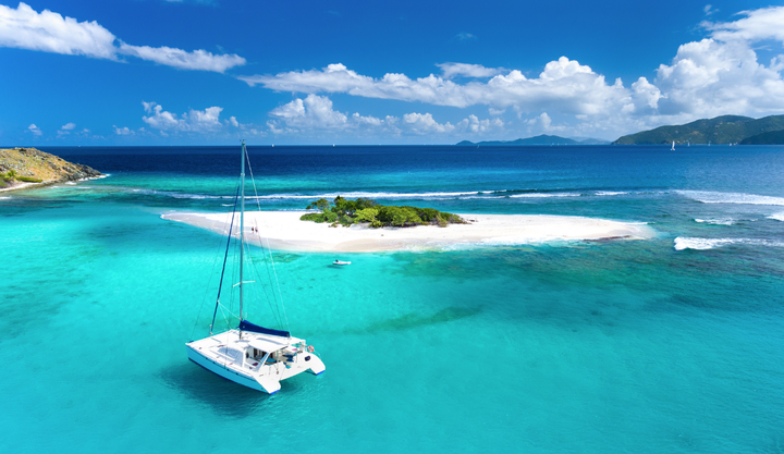 Catamaran anchored at Sandy Spit in British Virgin Islands in clear blue Caribbean waters.