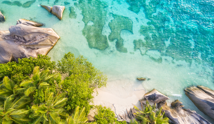 Looking down at a beautiful beach in Seychelles, with clear blue ocean waters and large rocks.