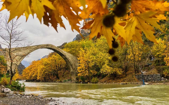 Bridge going across a river in Greece with October fall colors showing in the leaves.