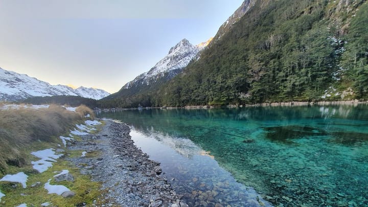 A clear Blue Lake in New Zealand surrounded by mountains.