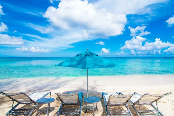 Beach chairs sitting under an umbrella on Grand Cayman's seven mile beach with clear blue waters.