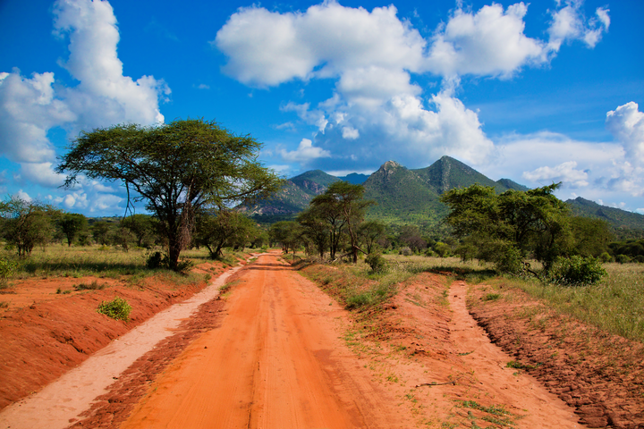 Kenya safari road with mountains and partly cloudy skies on a beautiful day.