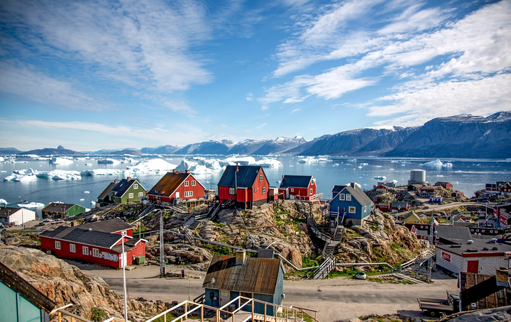 A village in Greenland with ice floating behind the homes in the sea, and mountains behind the ice.