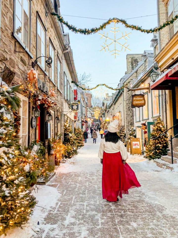 Christmas time in Old Quebec City with a woman walking streets lined with Christmas trees.